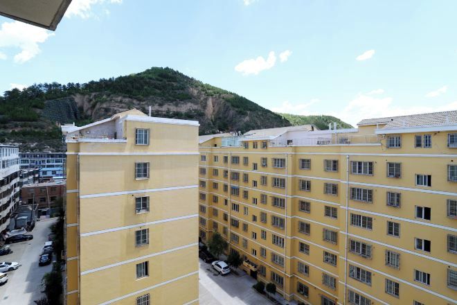 A multi-story yellow building with a flat roof, several windows, and a parking area in front.
