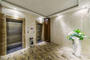 A hotel lobby with two elevators, a reception desk, and a decorative plant.