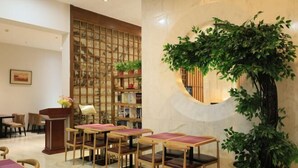 A restaurant with wooden tables and chairs, a decorative plant, and a bamboo screen wall. - Tangyue Hotel (Yan'an)