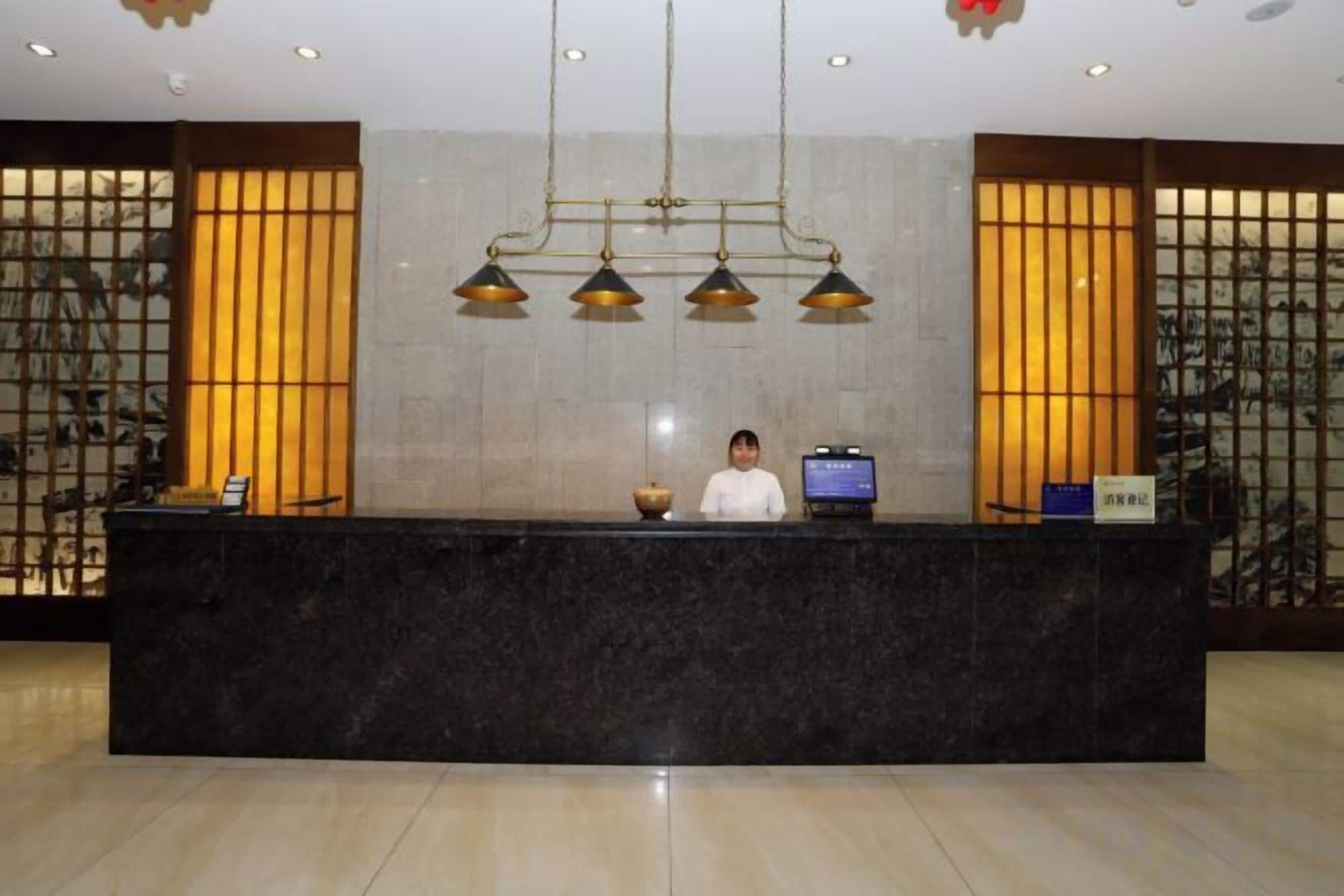 A reception desk with a person behind it, a computer, and a traditional decorative screen.