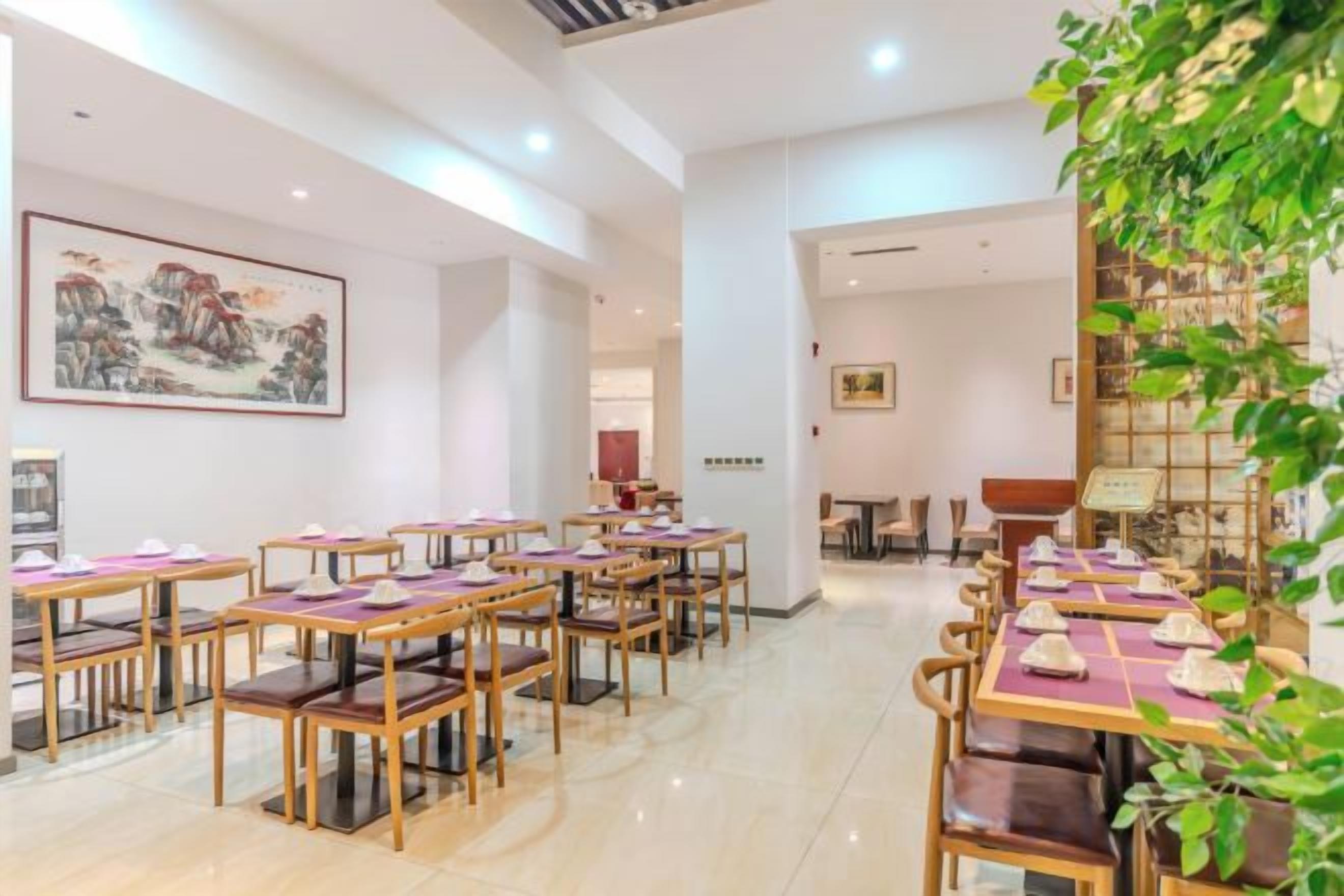 Une salle à manger d’hôtel avec plusieurs tables et chaises, un grand tableau au mur et une plante dans un coin.
