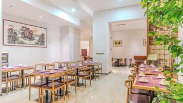 Une salle à manger d’hôtel avec plusieurs tables et chaises, un grand tableau au mur et une plante dans un coin.