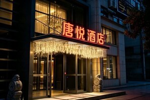A hotel entrance with a glass facade, a red sign, and a decorative light fixture above the doors.