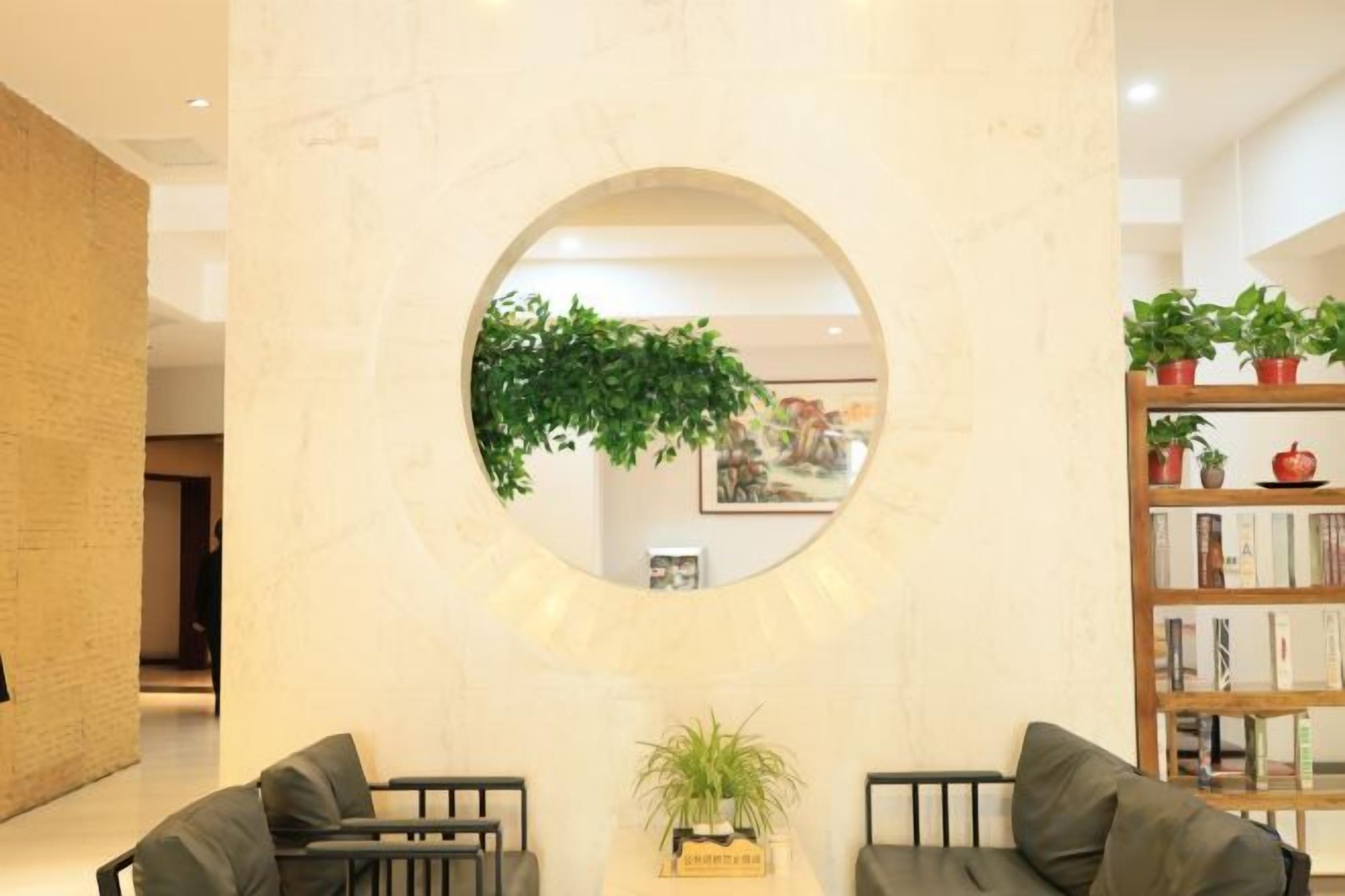 A lobby with a circular mirror, two sofas, a bookshelf, and a potted plant.