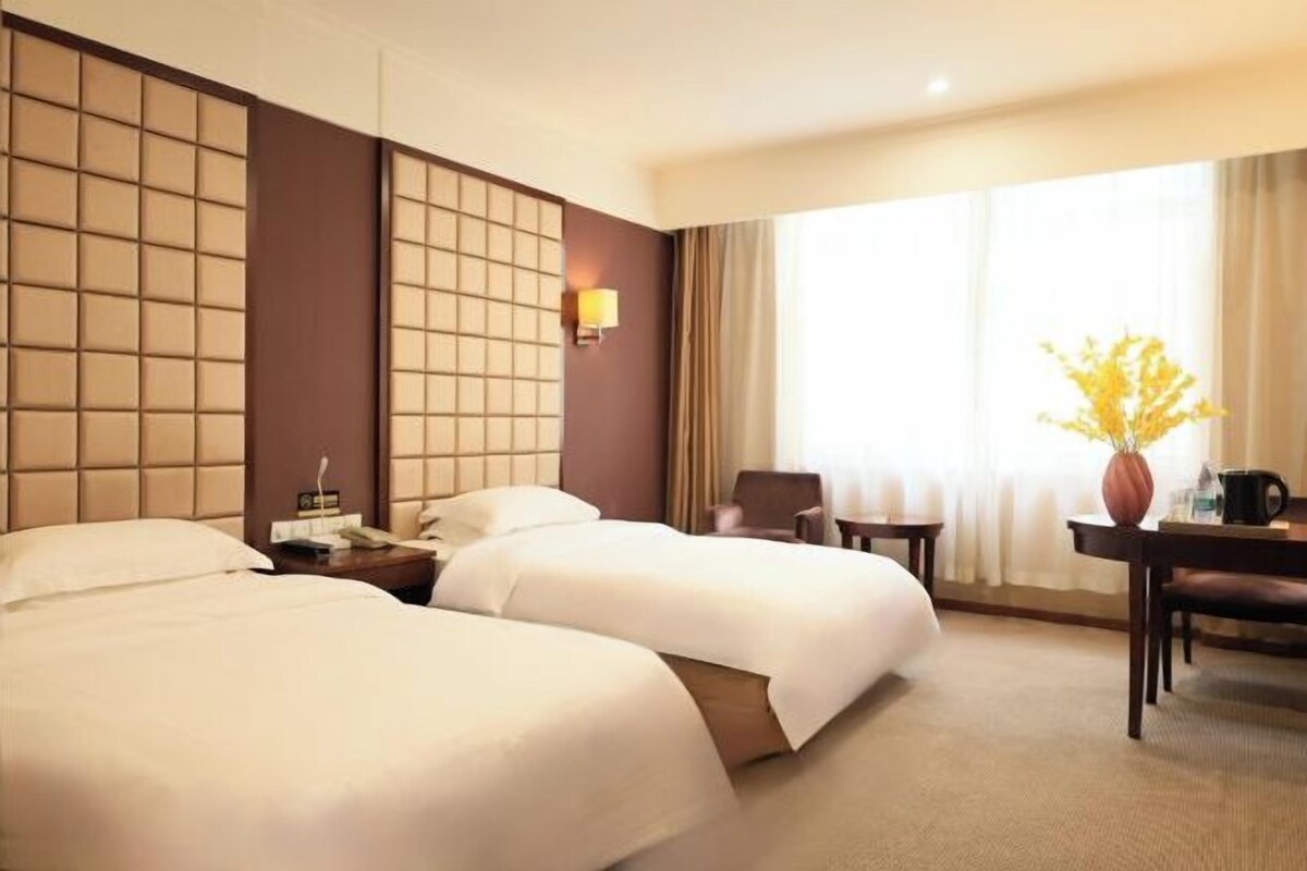 Habitación de hotel con dos camas, un escritorio, una silla, una lámpara y una ventana con cortinas.