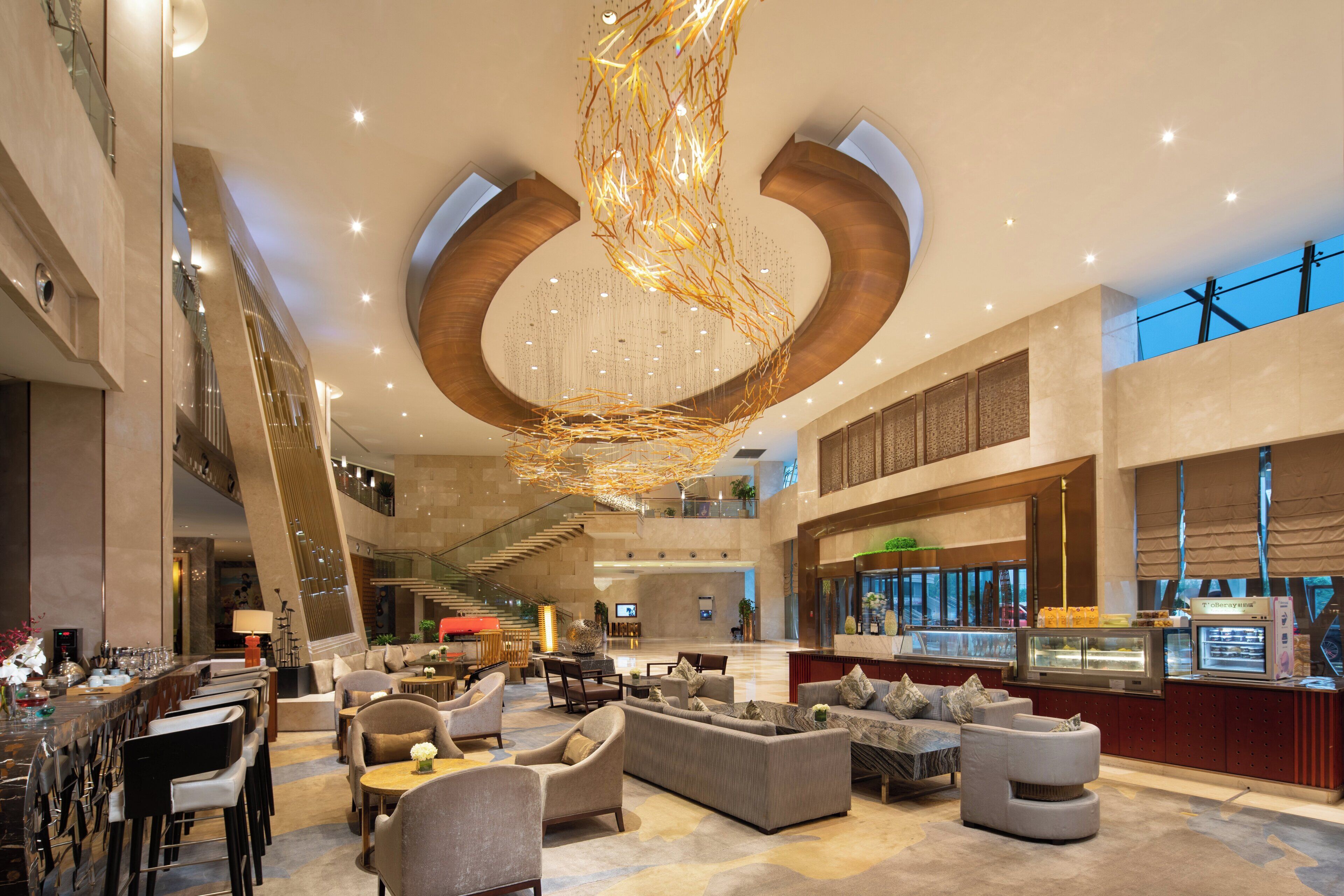 A spacious lobby with a modern chandelier, seating areas, and a visible staircase.
