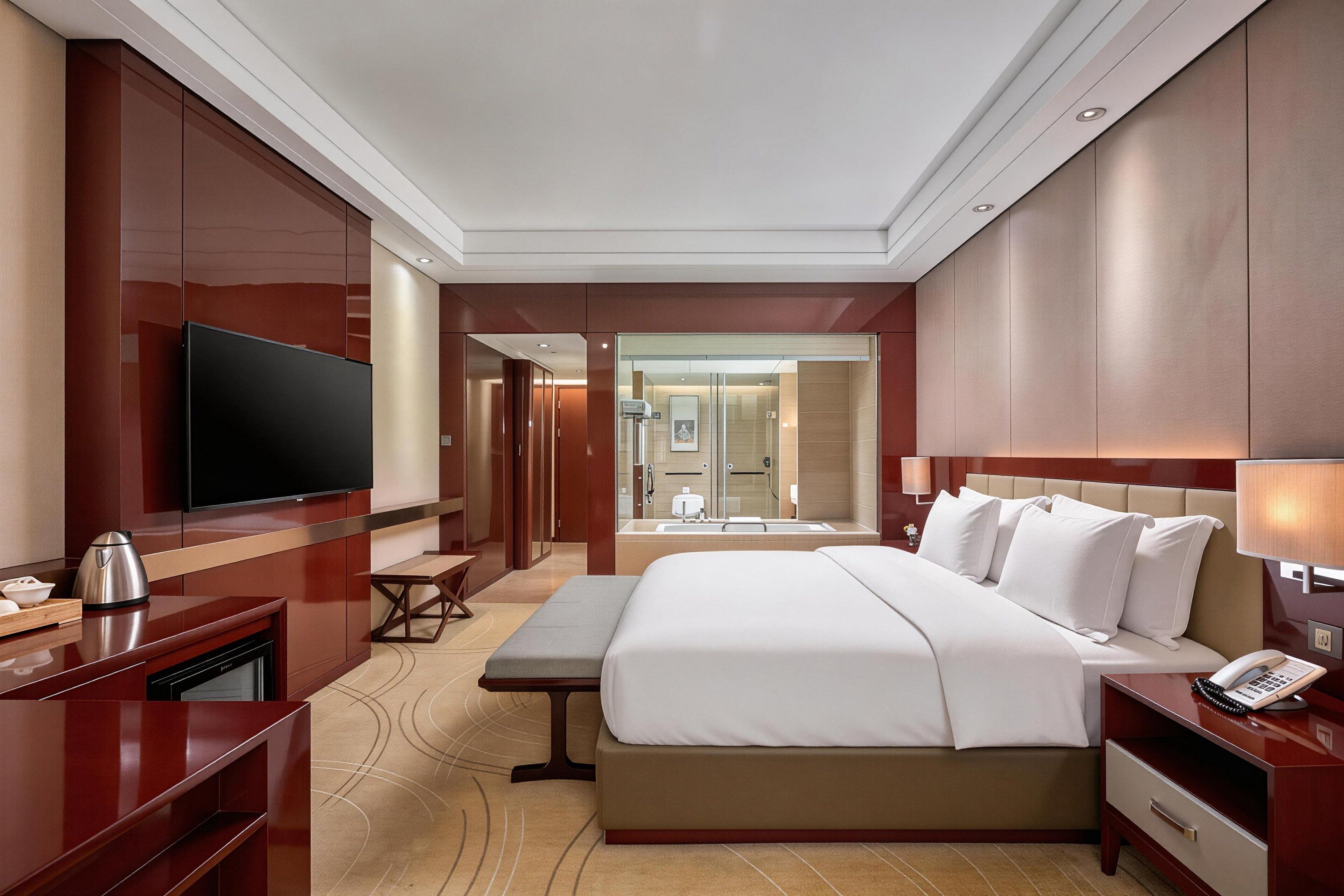A hotel room with a bed, bedside table, TV, and a bathroom visible through an open door.