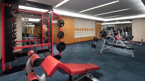 A gym with weightlifting equipment, a red bench, and a mirrored wall.