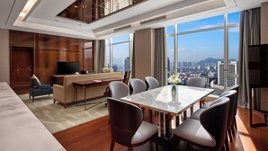 A modern hotel room with a dining area, a sofa, a TV, and a city view.