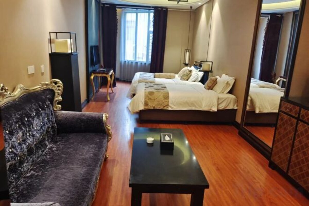 A hotel room with a sofa, two beds, a small table, and a mirror.