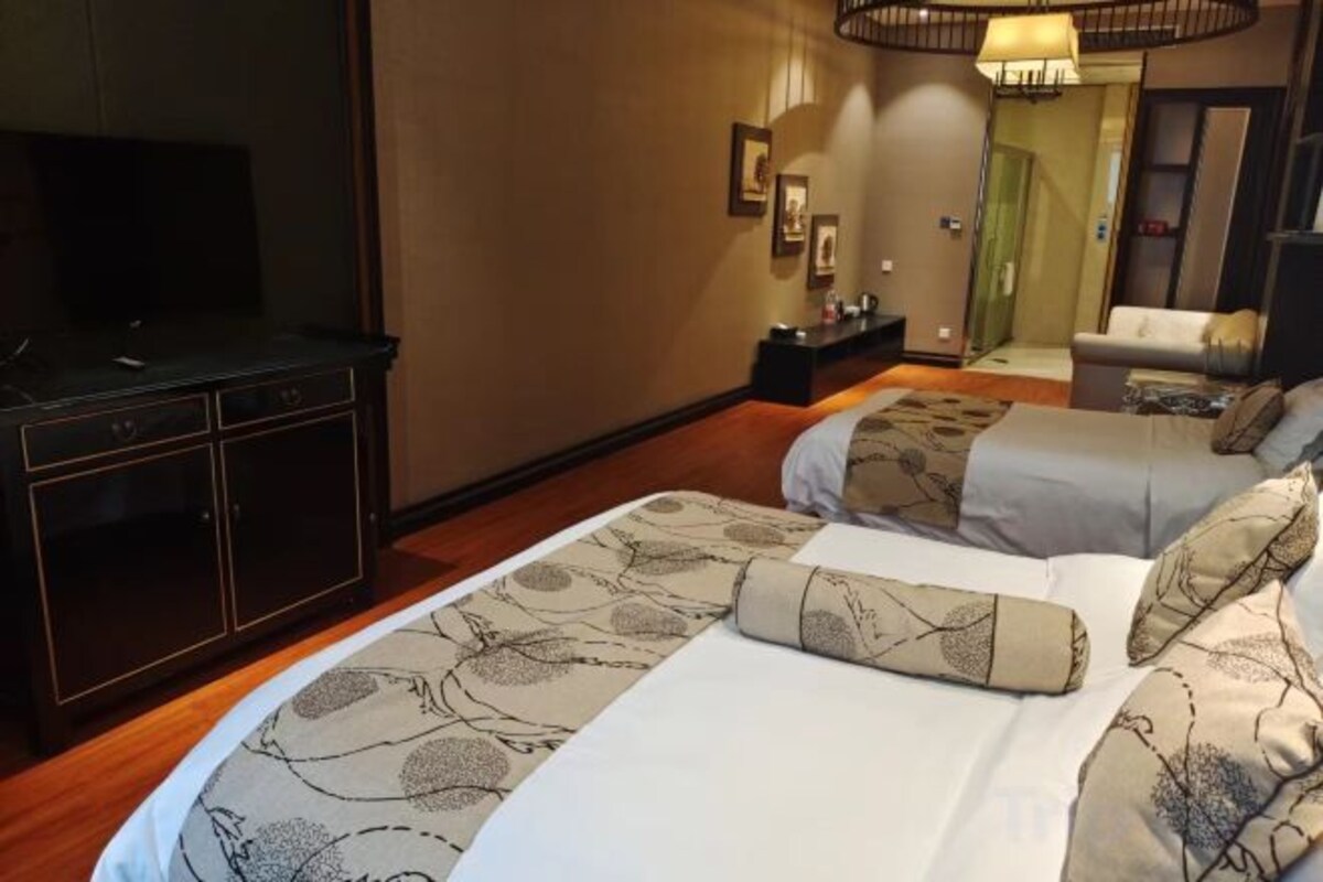 A hotel room with two beds, a TV, a desk, and a mirror.