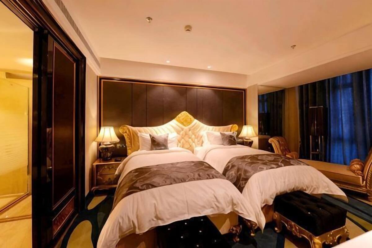 Ein Hotelzimmer mit einem großen Bett, zwei Nachttischen, einer Bank und einem großen Spiegel.