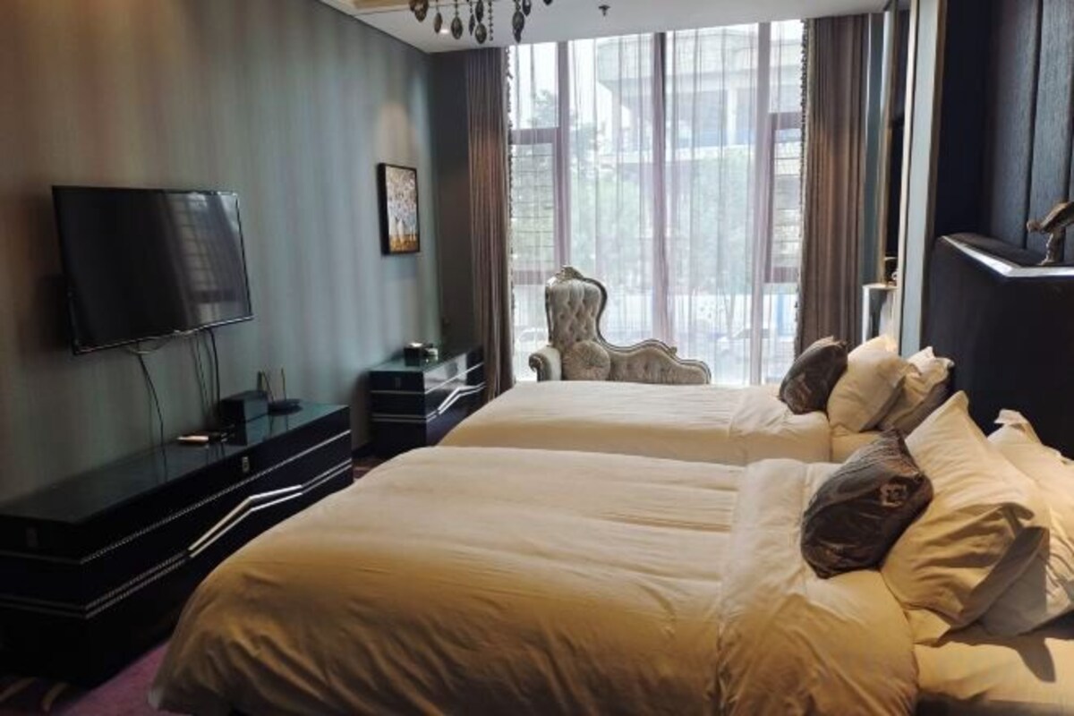 A hotel room with two beds, a flat-screen TV, a chair, and a large window.