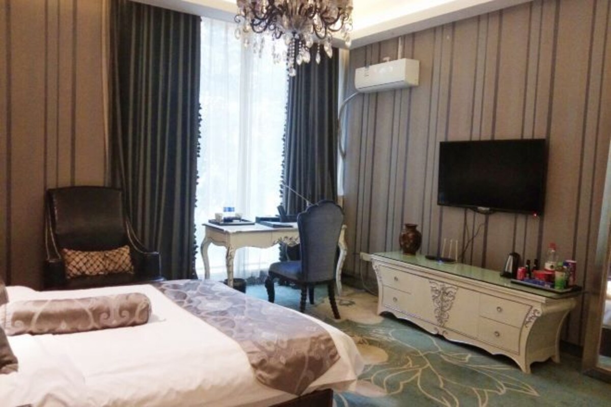A hotel room with a bed, a desk, a television, and a dresser.