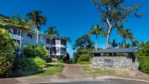 A residential building with a stone wall entrance, a pathway leading to the main entrance, and a view of the ocean. - Oasis 26 (Whitsundays)