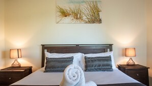 A neatly made bed with two pillows, a rolled towel, and two bedside lamps on wooden nightstands. - Oasis 26 (Whitsundays)