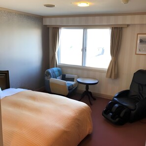 Une chambre d’hôtel avec un lit, un fauteuil massant, une petite table et une fenêtre avec des rideaux.