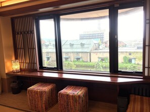 A room with a large window, a wooden bench, and two colorful woven stools. - Otaru Furukawa Hotel (Otaru)