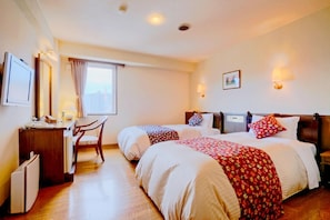 Une chambre d’hôtel avec deux lits, un bureau, une chaise, un radiateur et une fenêtre avec des rideaux.