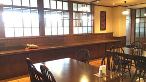L’intérieur d’un restaurant, avec des tables et des chaises en bois, de grandes fenêtres et un coin bar.