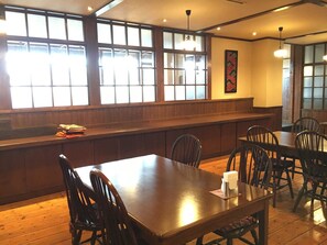 L’intérieur d ’un restaurant, avec des tables et des chaises en bois, de grandes fenêtres et un coin bar.