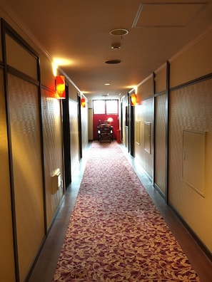 Un couloir d’hôtel avec un tapis à motifs, des portes et des appliques murales.