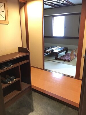 A traditional Japanese room with tatami flooring, a low wooden table, a cushioned bench, and a shelf with slippers. - Otaru Furukawa Hotel (Otaru)