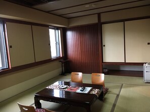 Ein traditioneller japanischer Raum mit Tatami-Bodenbelag, einem niedrigen Holztisch mit Kissen und Schiebetüren.