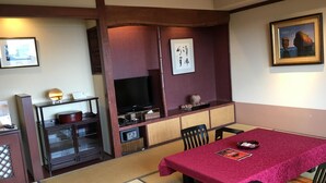 Una habitación tradicional japonesa con suelo de tatami, una mesa baja con mantel rojo, un televisor y un cuadro en la pared.