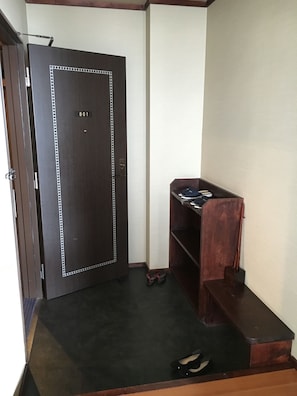A room with a dark wooden door marked with the number 801, a small wooden desk with a chair, and a pair of shoes on the floor.