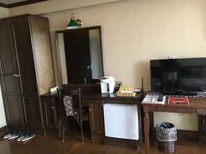 Une pièce de taille modeste, comprenant un bureau en bois, un petit réfrigérateur, une télévision et une chaise.