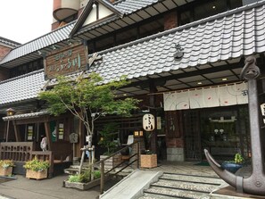 Un bâtiment japonais traditionnel, avec un toit recouvert de tuiles, une enseigne en bois et une lanterne en pierre.