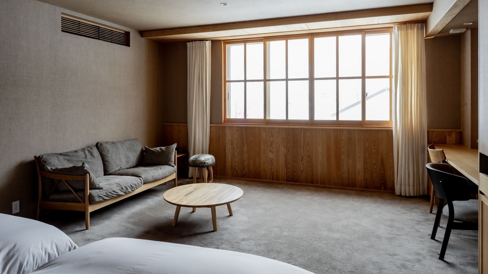 Ein Zimmer mit einer Couch, einem runden Tisch, einem Sessel und einem großen Fenster mit Vorhängen.