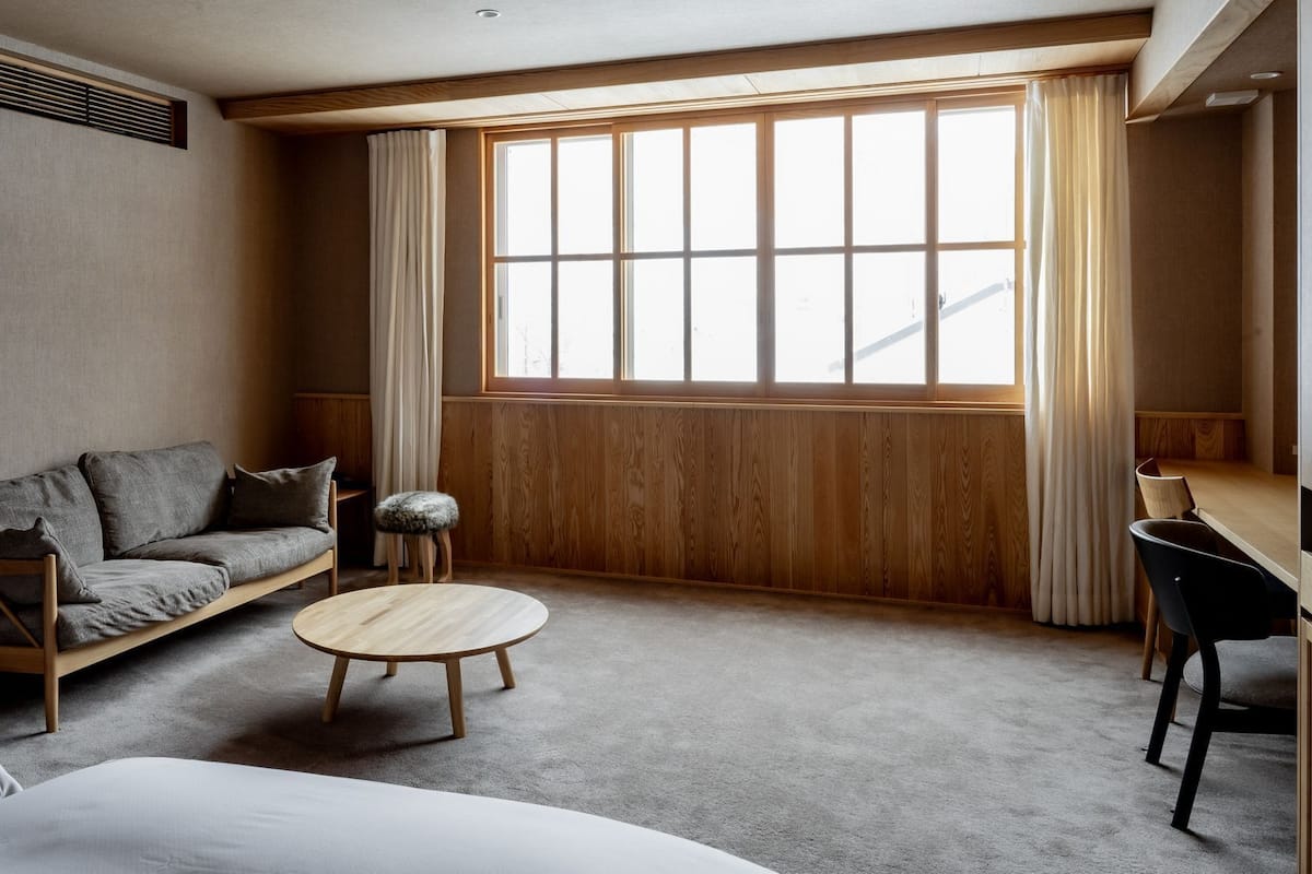 A room with a sofa, a round table, a chair, and a large window with curtains.