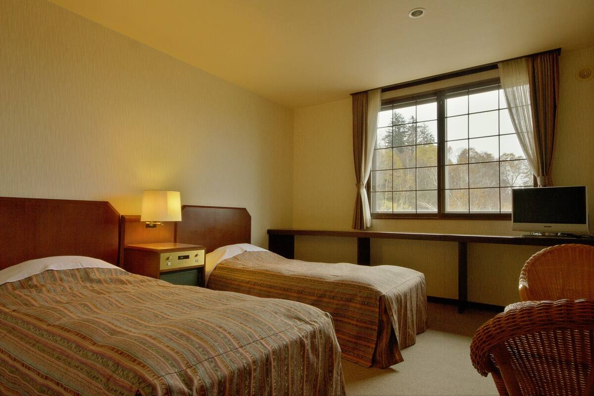 A hotel room with two beds, a desk with a television, and a window with curtains.