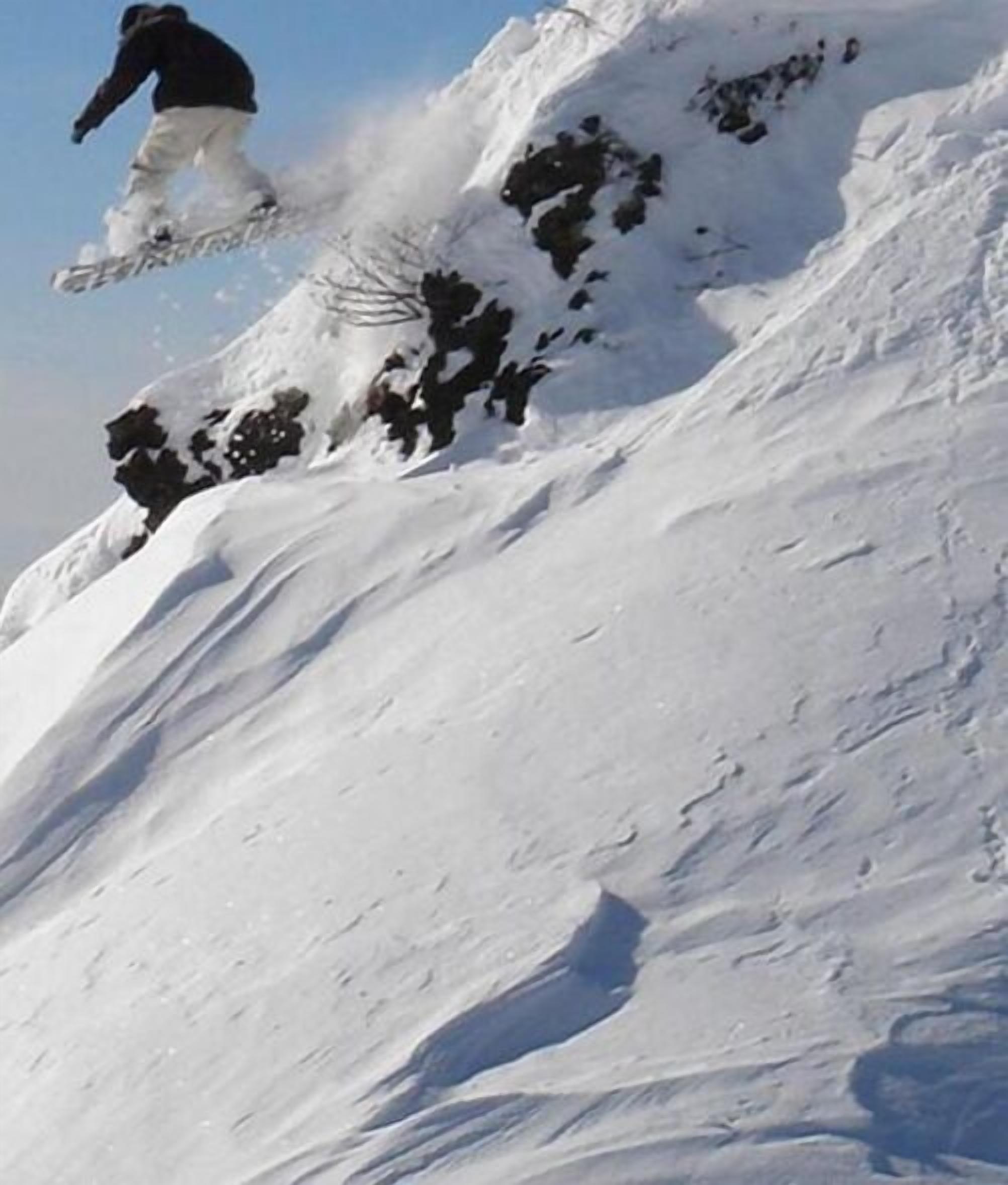 A snowboarder mid-air performing a jump on a snowy slope.