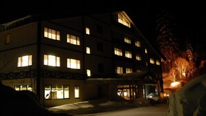 Ein mehrgeschossiges Gebäude mit beleuchteten Fenstern, verschneitem Untergrund und einem sichtbaren Eingang.