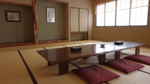 Ein Raum mit Tatami-Matten, einem niedrigen Holztisch, Kissen und verschiebbaren Türen.