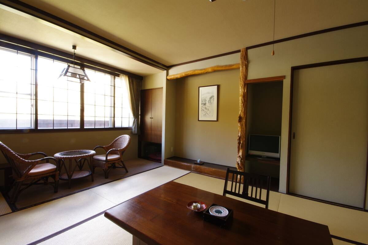A traditional Japanese room with tatami flooring, a wooden table, and a TV on a stand.