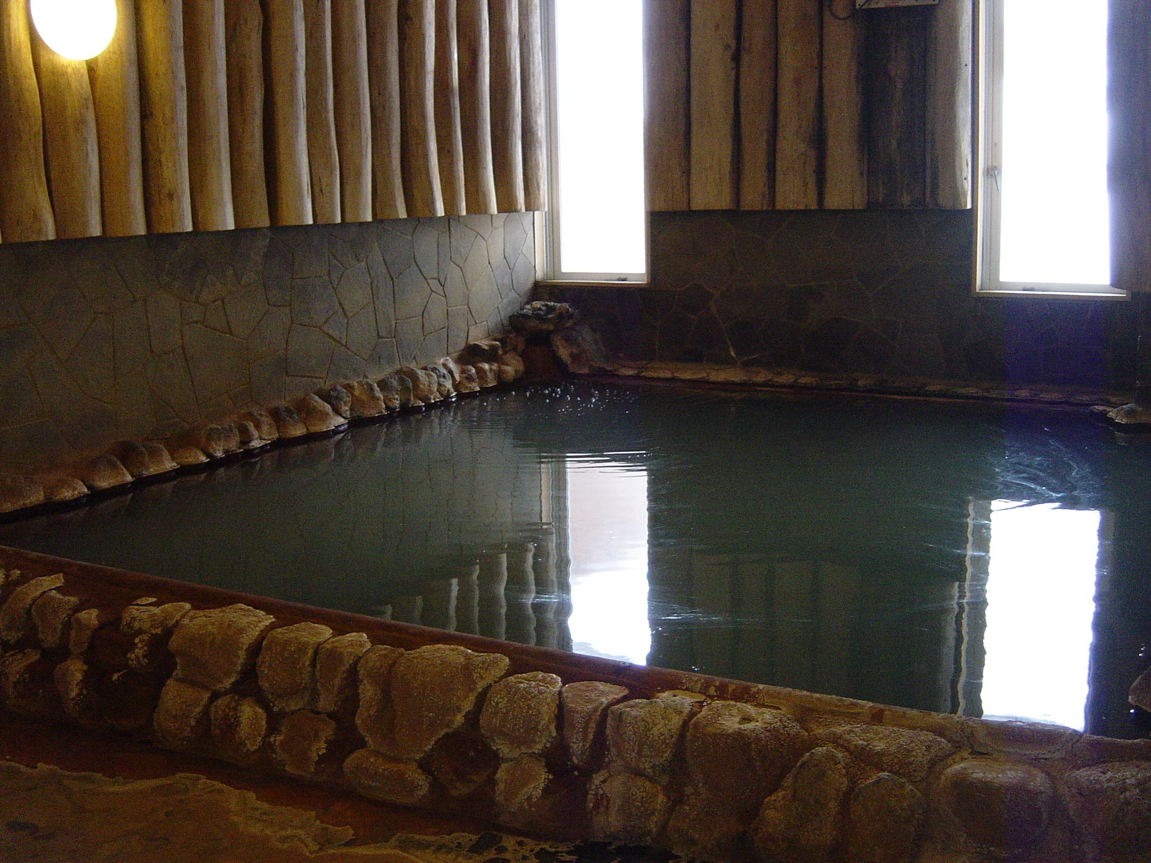 A stone-lined pool with a stone border and a wooden wall with vertical slats.