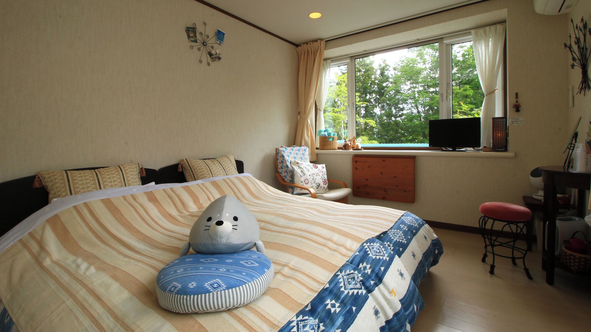 A bedroom with a large bed, a chair, a desk, a TV, and a window with a view of trees.