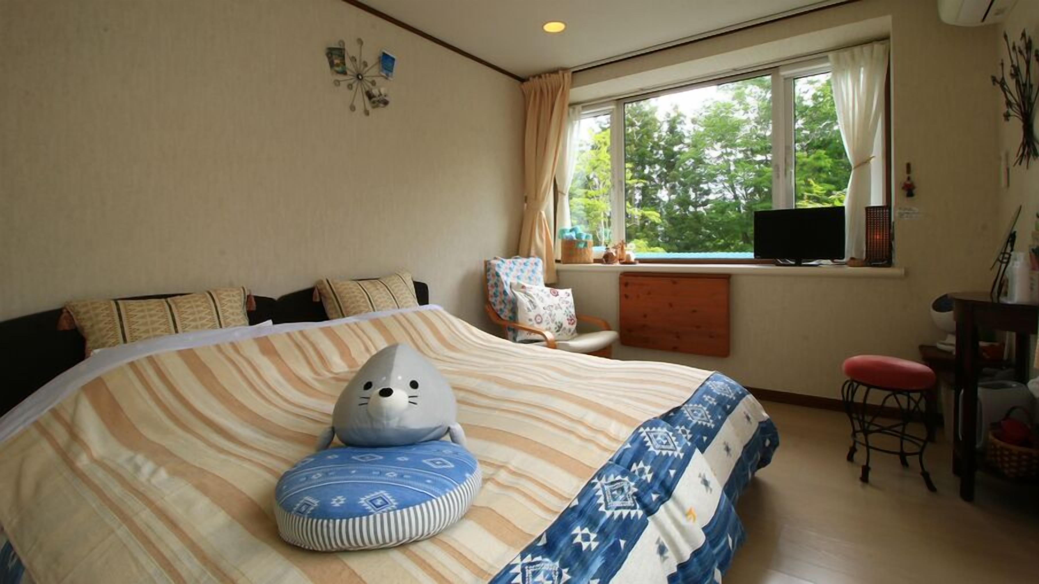 A bedroom with a large bed, a chair, a television, and a window with a view of trees.