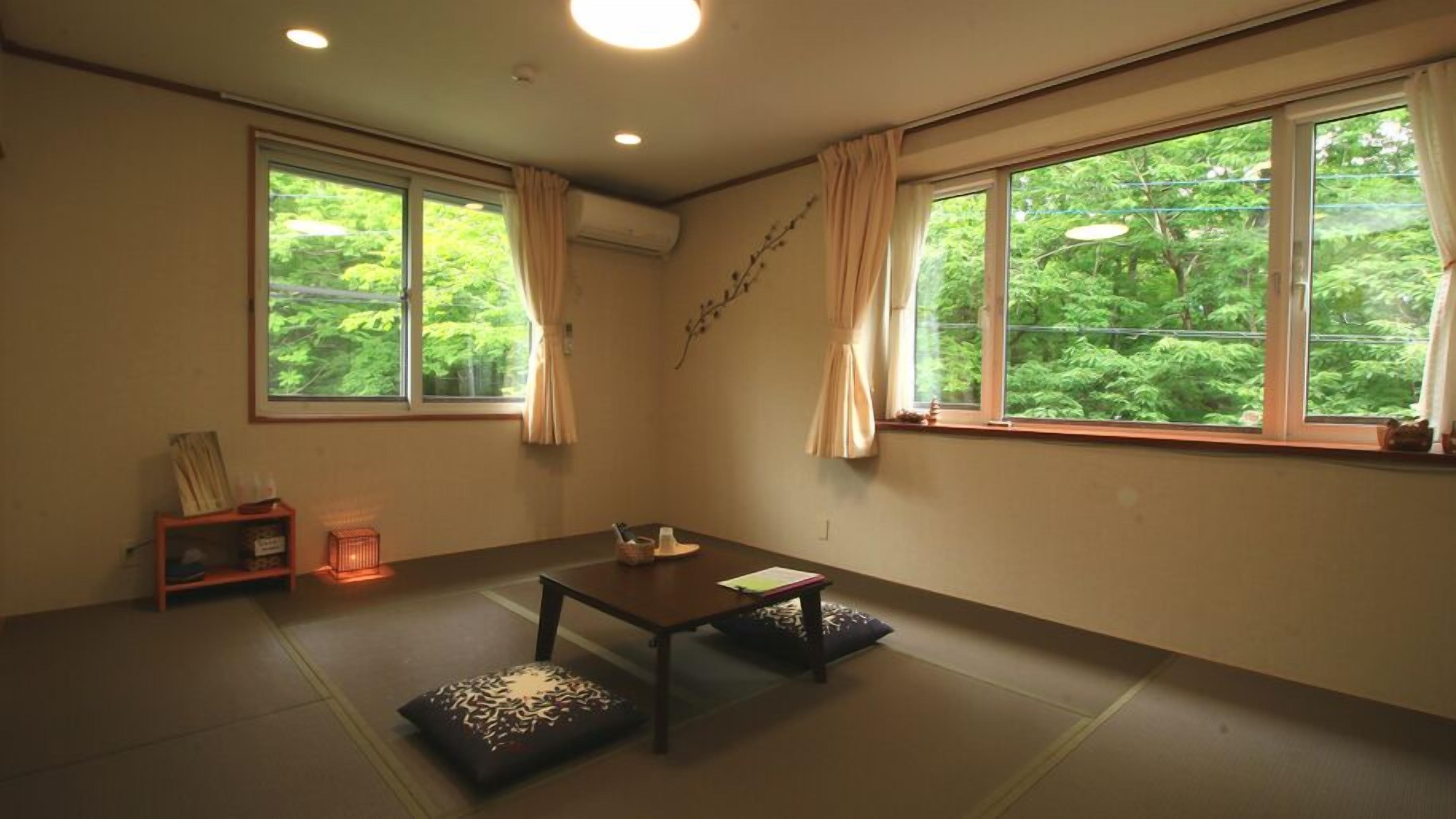 A room with tatami mats, a low table, a shelf with items, and large windows with curtains.