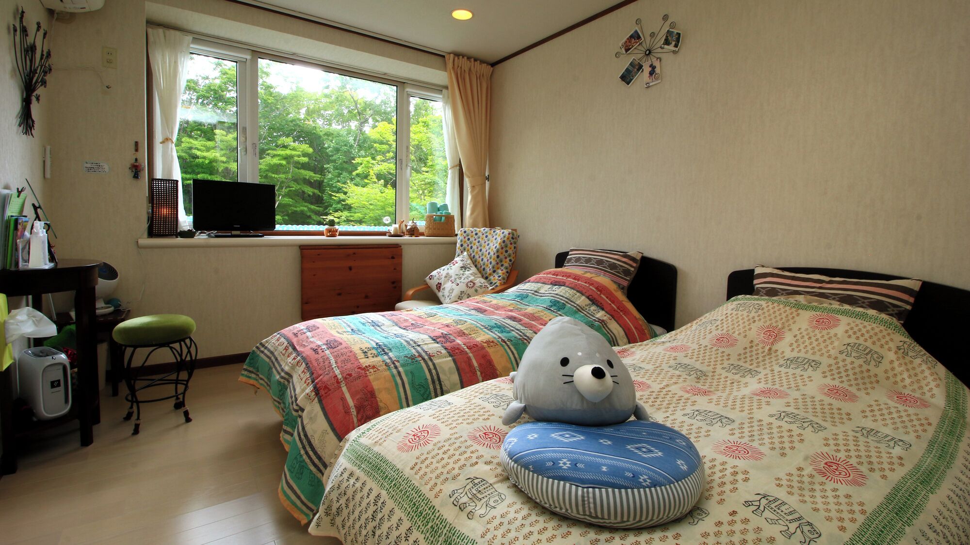 A bedroom with two beds, a desk, a chair, and a window with a view of trees.