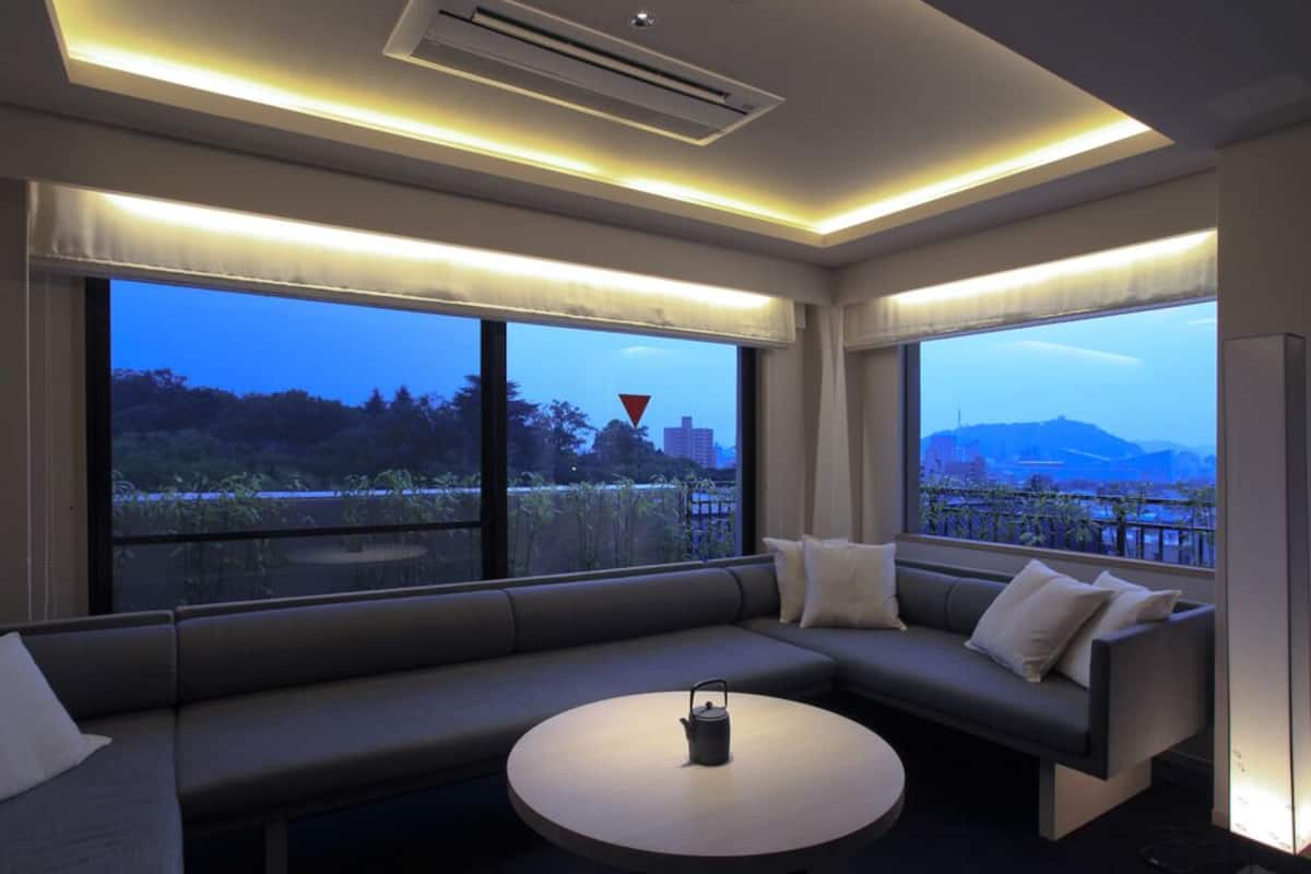 Een moderne hotelkamer met een bank, een ronde tafel en grote ramen met uitzicht over de stad.