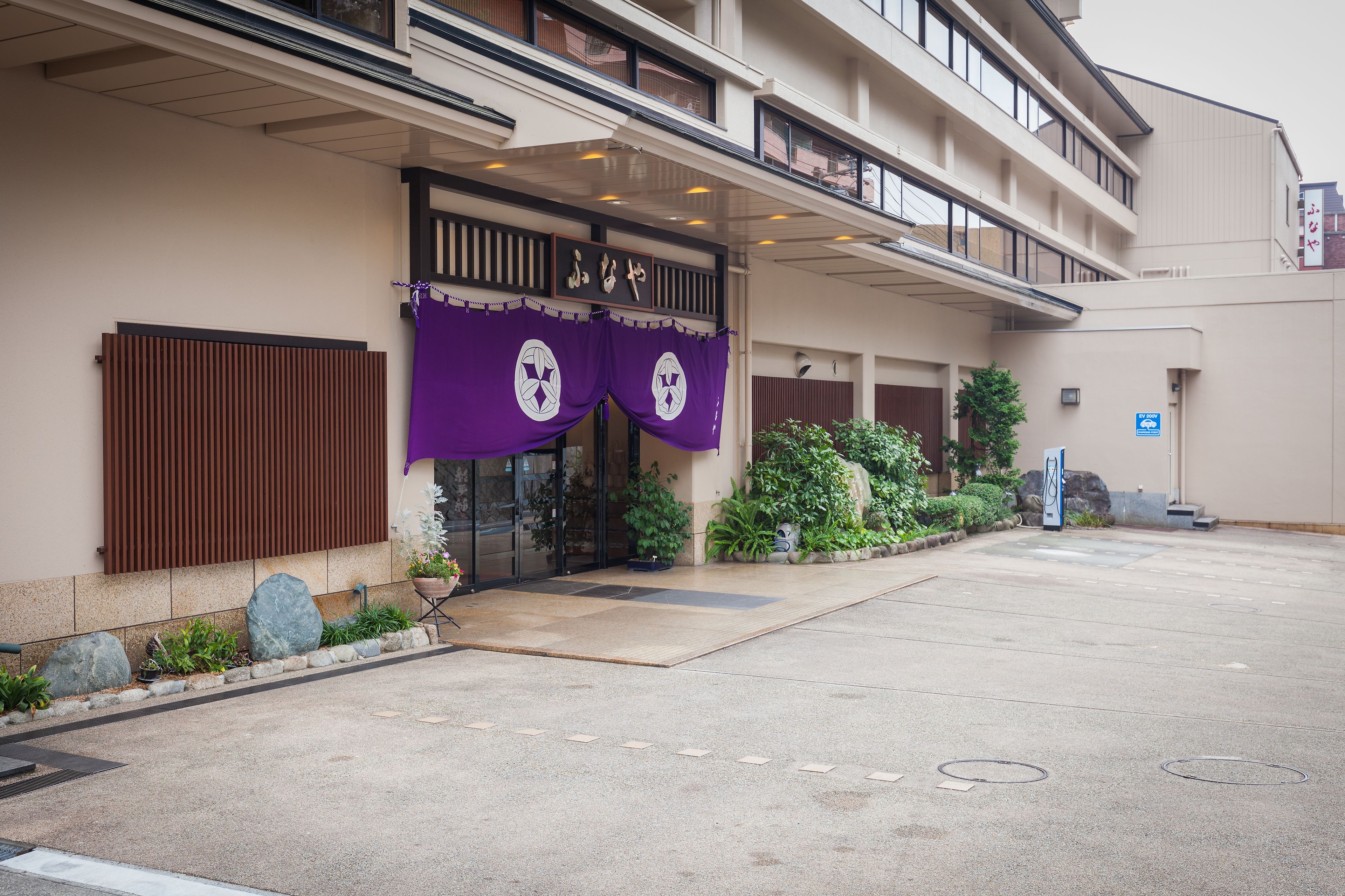 A hotel entrance with a covered walkway, potted plants, and a signboard.