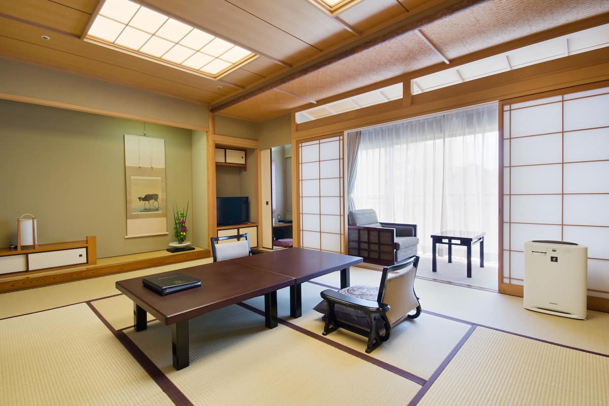 Een traditionele Japanse kamer met tatami vloerbedekking, een lage tafel met kussens, een televisie, schuifdeuren en een kleine koelkast.