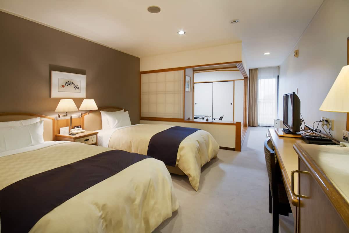 Een hotelkamer met twee bedden, een bureau met een computer en een televisie.