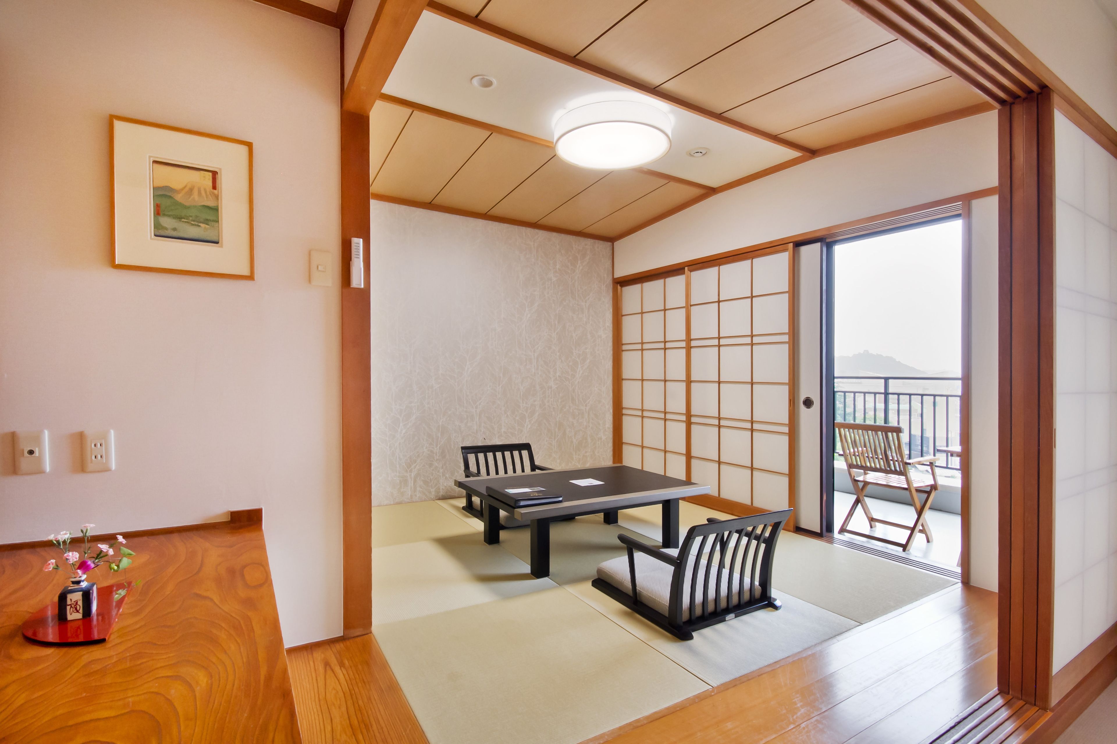 Une pièce de style japonais traditionnel, avec un sol recouvert de tatamis, une porte coulissante, une table entourée de chaises et une vue sur les montagnes, visible à travers la porte.