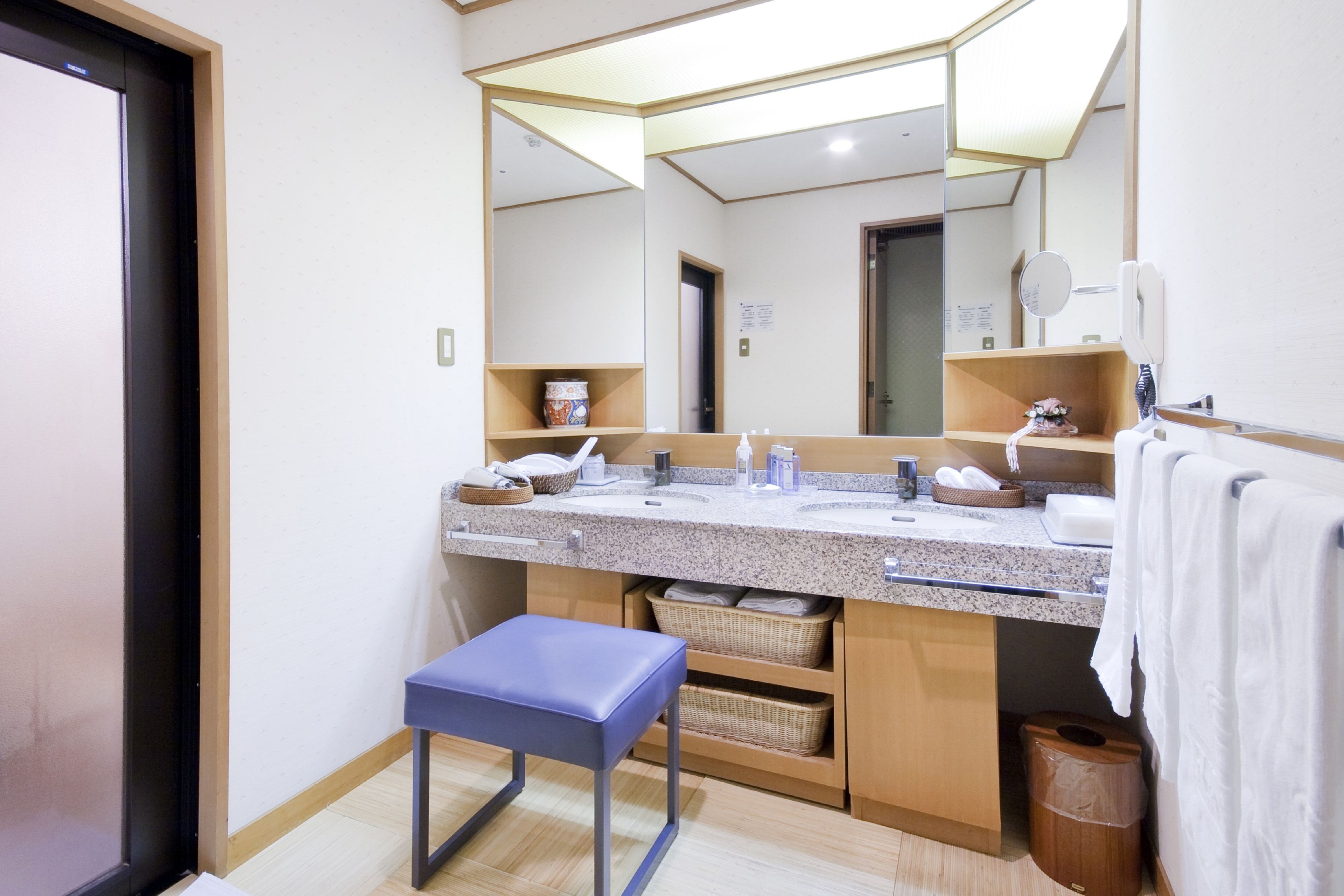 A modern bathroom with a large mirror, two sinks, a blue bench, and storage baskets.